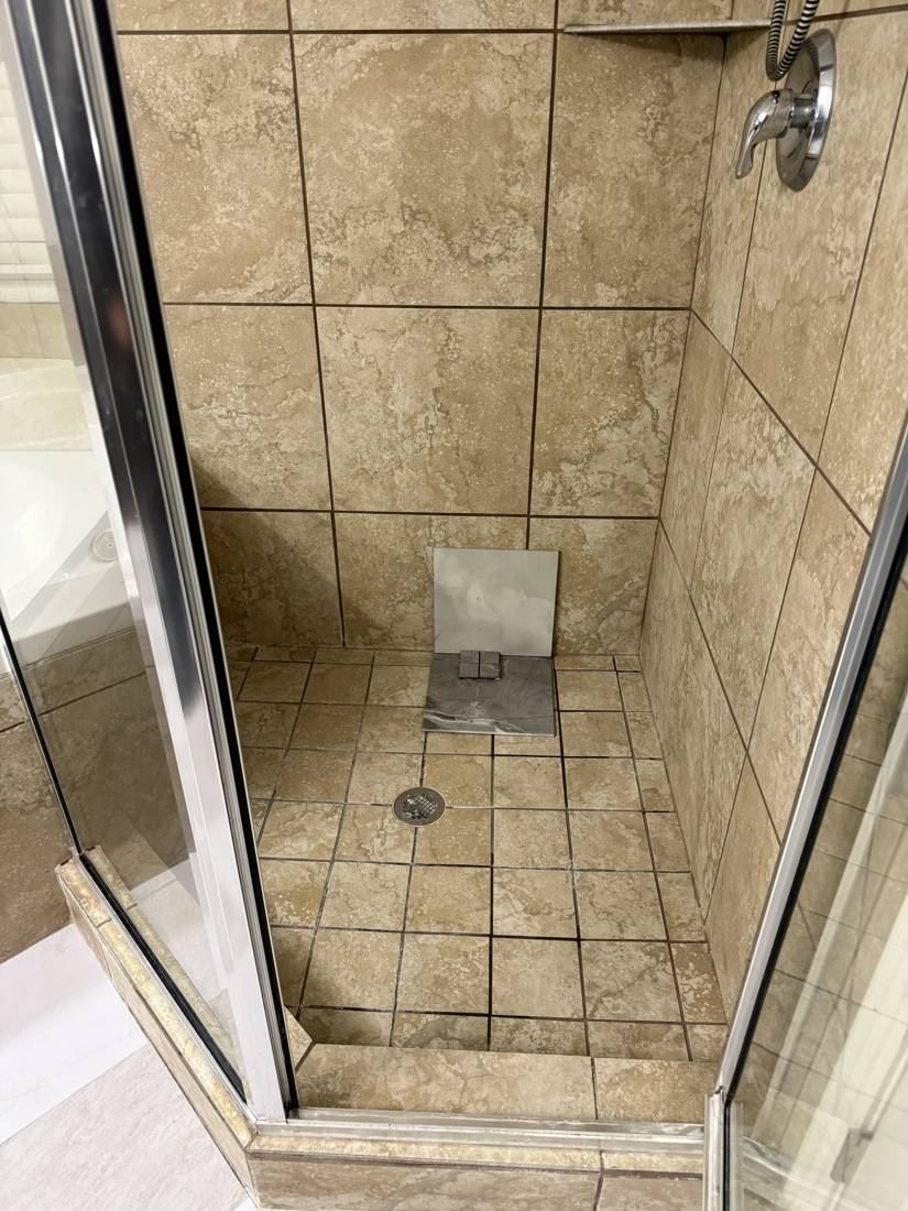 The original corner shower with tan tile and a glass door, before demolition