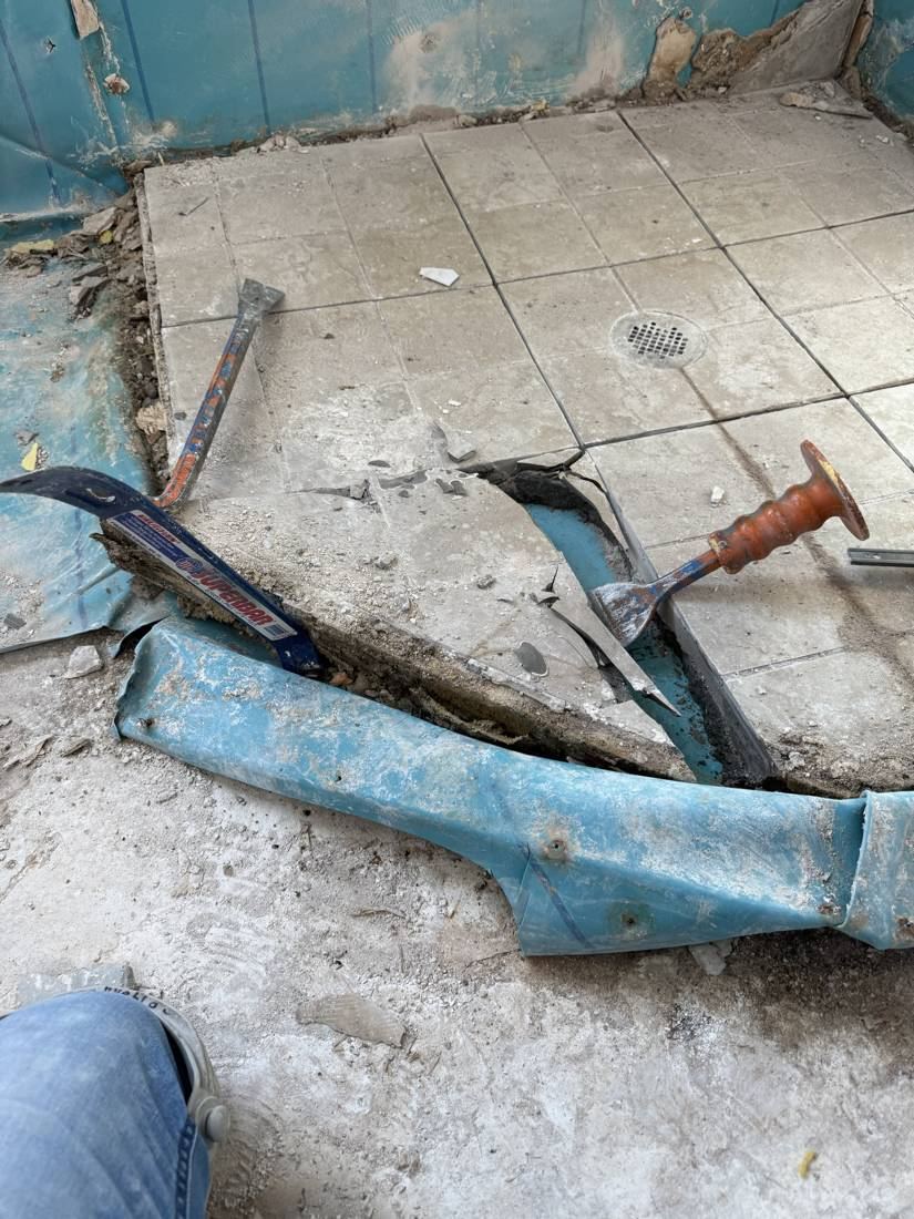 Blue pan liner pulled back from the broken-up shower floor during demolition