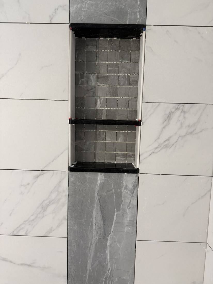 Tiled shower niche with two black shelves and a mosaic back, set in a gray accent strip