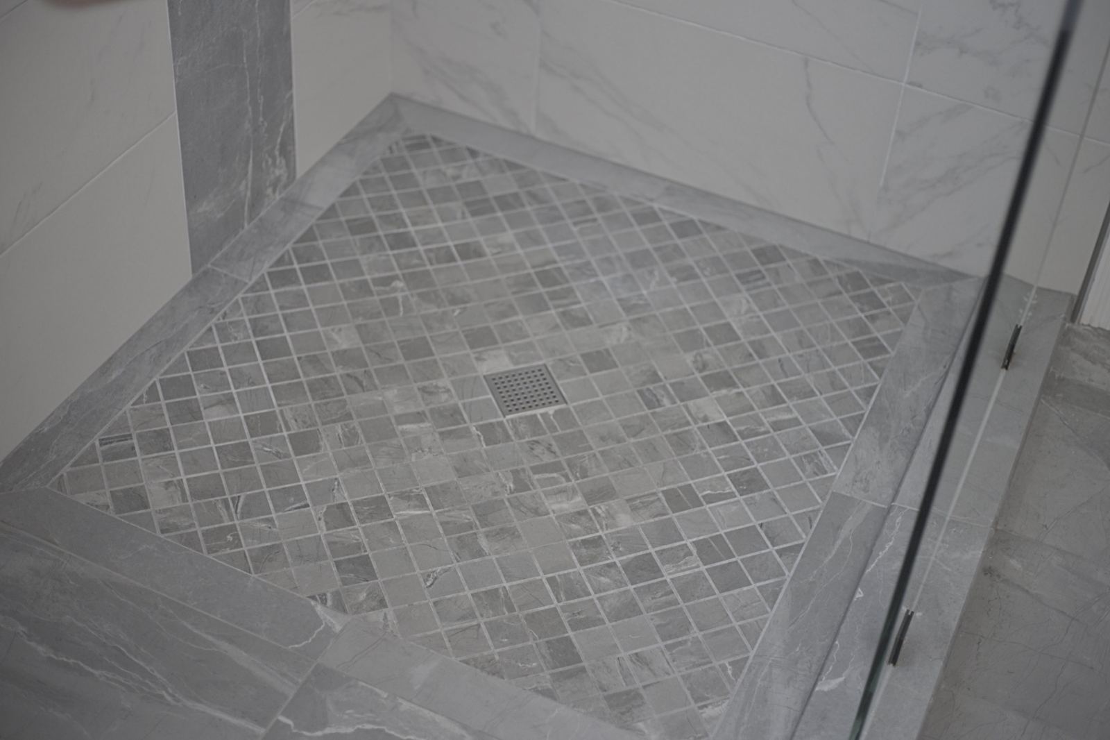 Finished shower floor: gray diagonal mosaic tile with a mitered stone-look border and a square stainless drain