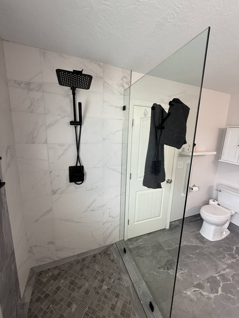 Finished shower with white marble-look wall tile, a black shower set, mosaic floor and frameless glass panel