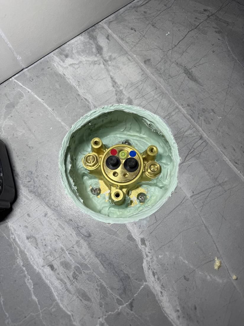 Brass valve body sealed in a ring of green waterproofing in the tile floor