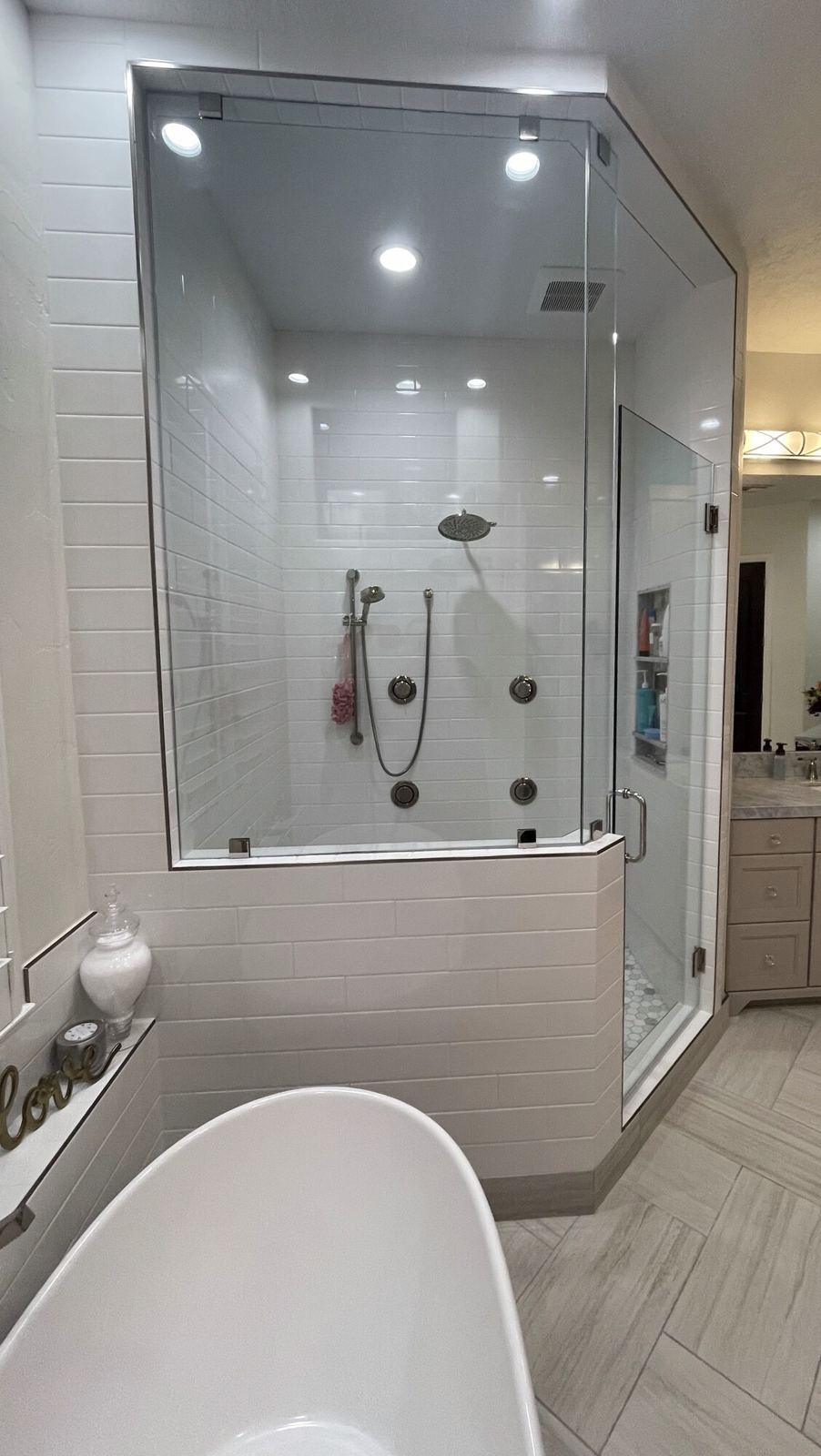 Corner shower with a frameless glass enclosure and white wall tile, beside a freestanding tub