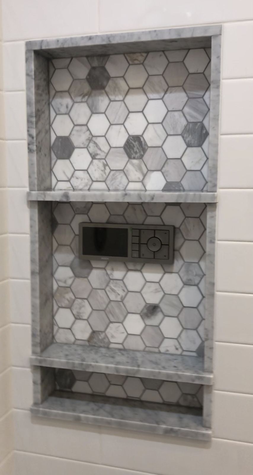Tall shower niche with marble trim, two marble shelves and a hexagon marble mosaic back, with a digital shower control set into it
