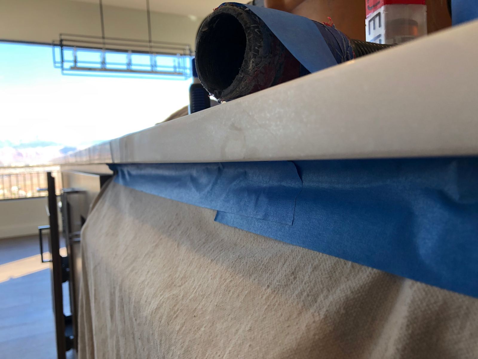 Countertop edge with the cabinets below covered in a canvas drop cloth taped along the underside, and a dust-collection hose on the counter