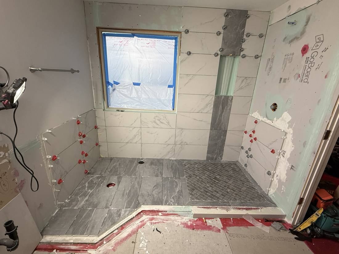 Large-format wall tile going up in the shower with a niche and accent strip